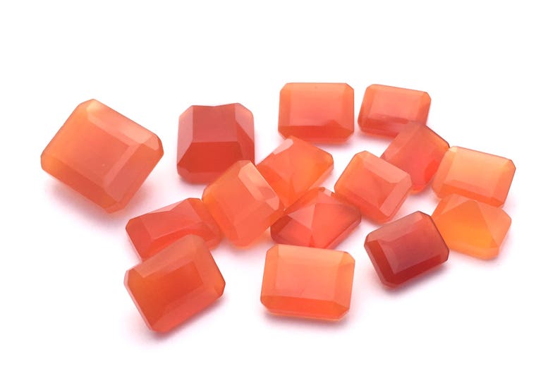 Puede incluir: Una colecci&oacute;n de 14 piedras preciosas de cornalina naranja, talladas en forma rectangular. Las piedras preciosas est&aacute;n dispuestas en un mont&oacute;n suelto sobre un fondo blanco.