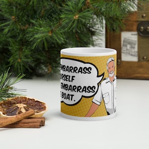 May include: White ceramic mug with a comic book style illustration of a man with a white beard and a white captain's hat. The text on the mug reads "Embarrass Yourself Embarrass the Boat."