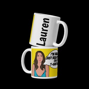 May include: White ceramic mug with a yellow background and a pop art style illustration of a woman with brown hair and a blue top. The text "I've really just been focusing on my t-shirt" is in a speech bubble above her head. The mug also has the name "Lauren" written on the side.