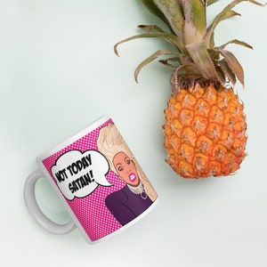 May include: White ceramic mug with a pink and white polka dot background. The mug features a cartoon image of a woman with blonde hair and a purple shirt. The text "NOT TODAY SATAN!" is in a speech bubble above her head.
