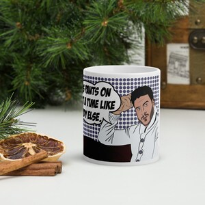 May include: White ceramic mug with a pop art design featuring a man with a beard and the text "Getting pants on at a time like this, nobody else."
