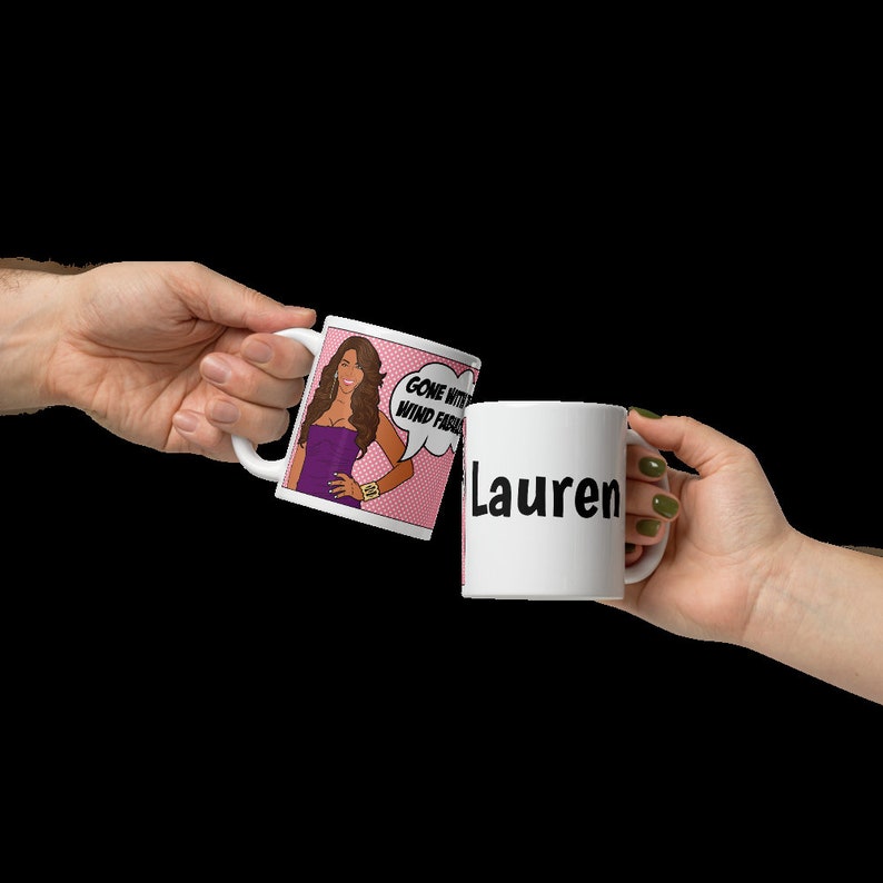 May include: Two white ceramic mugs. One mug has a pink and white comic book style image of a woman with the text "Gone With The Wind Fashion". The other mug has the name "Lauren" in black text.