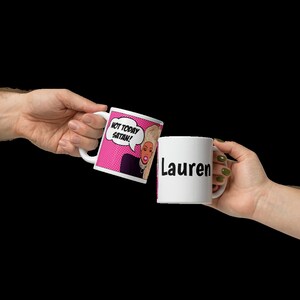 May include: Two white ceramic mugs. One mug has a pink background with a cartoon image of a woman with blonde hair and the text "Not today Satan!" The other mug has the name "Lauren" printed in black.