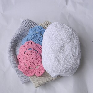 May include: A pile of crocheted items including a white ball of yarn, a gray crocheted hat, and two doilies, one pink and one blue.
