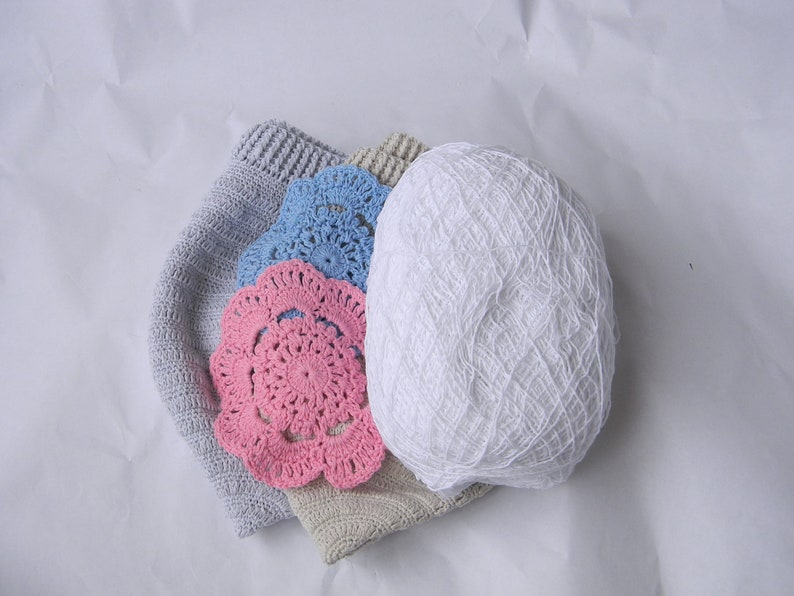 May include: A pile of crocheted items including a white ball of yarn, a gray crocheted hat, and two doilies, one pink and one blue.