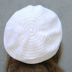 May include: White crocheted beret with a circular pattern.