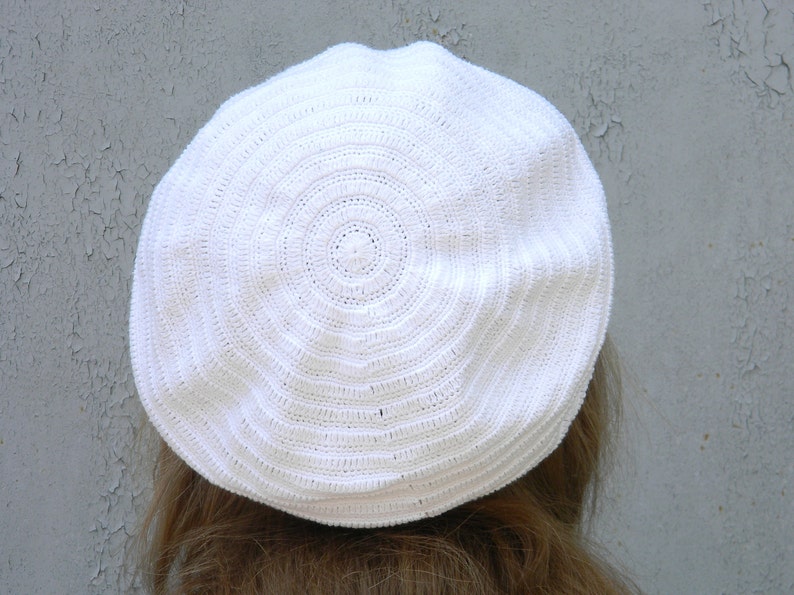 May include: White crocheted beret with a circular pattern.