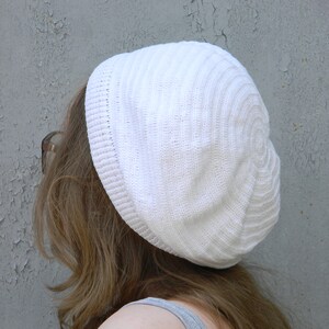 May include: A white knitted beanie with a ribbed texture. The beanie is worn on a person's head.