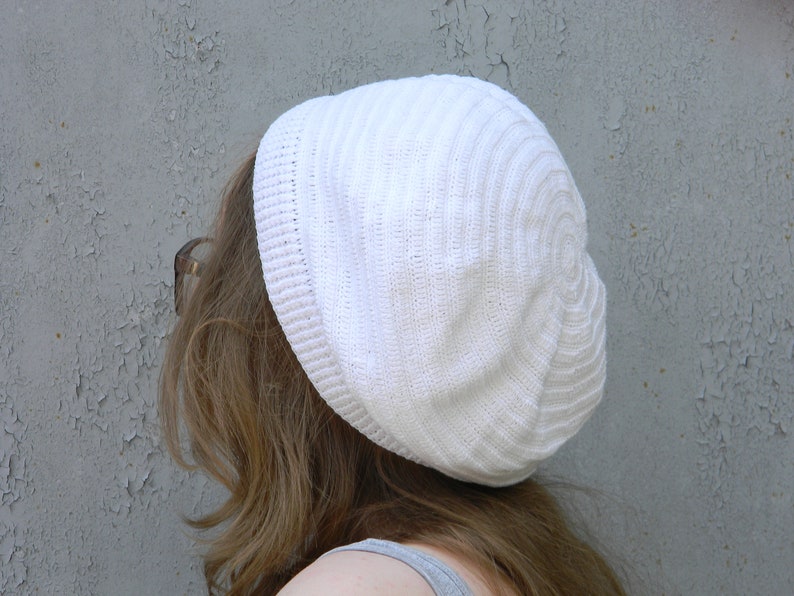 May include: A white knitted beanie with a ribbed texture. The beanie is worn on a person's head.