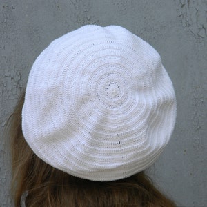 May include: A white crocheted beret with a circular pattern.