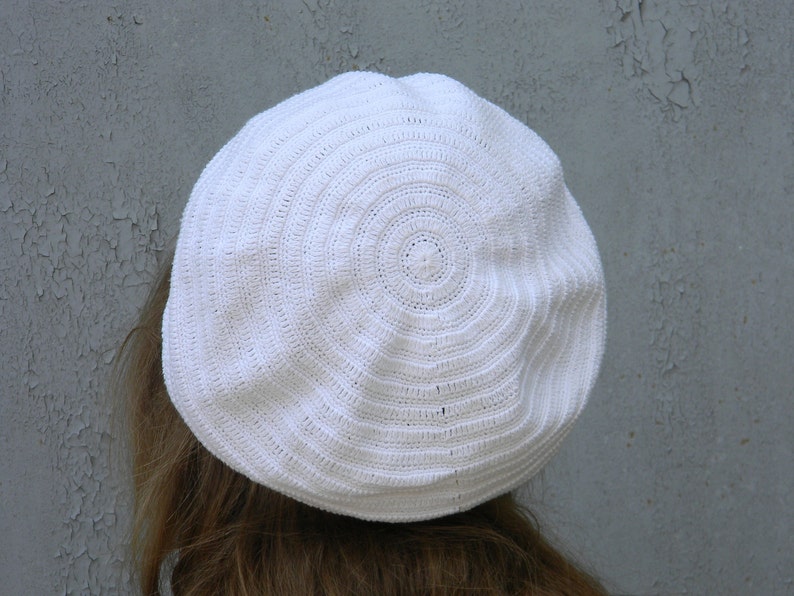 May include: A white crocheted beret with a circular pattern.