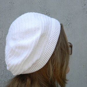May include: A white crocheted beanie with a ribbed texture. The beanie is worn on a person's head.