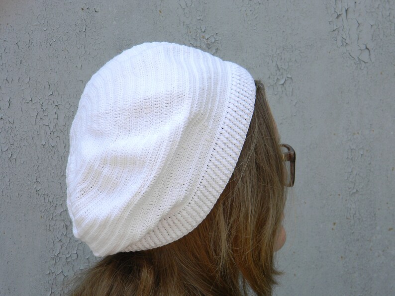 May include: A white crocheted beanie with a ribbed texture. The beanie is worn on a person's head.