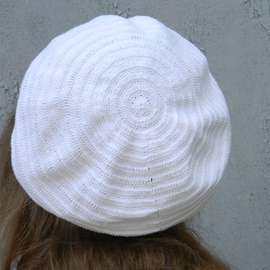 May include: A white crocheted beret with a circular pattern.