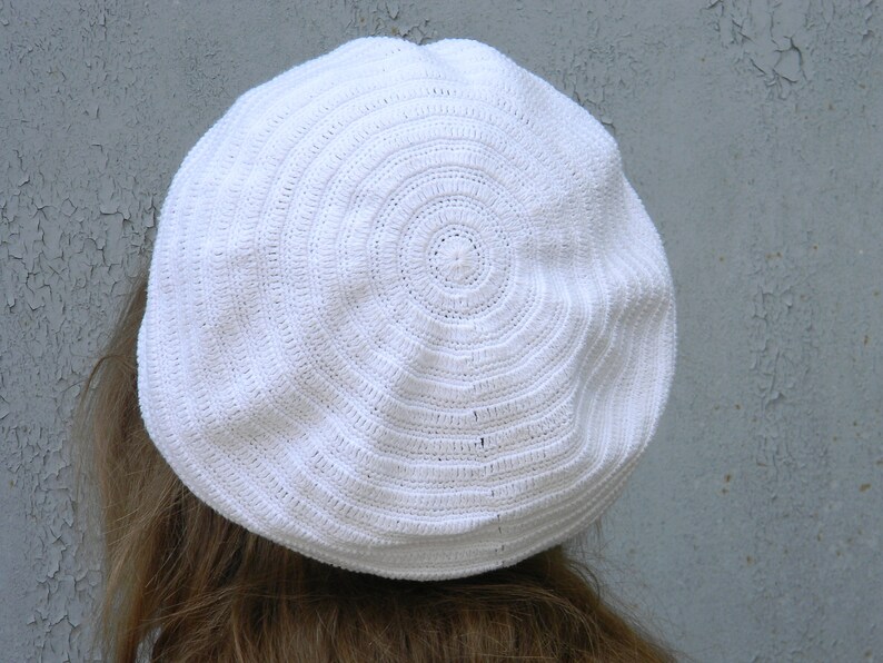 May include: A white crocheted beret with a circular pattern.