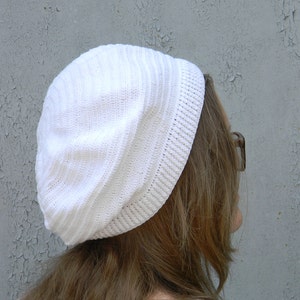 May include: A white knitted beanie with a ribbed texture. The beanie is slouchy and has a folded brim.