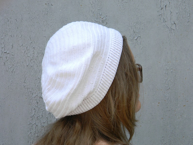 May include: A white knitted beanie with a ribbed texture. The beanie is slouchy and has a folded brim.