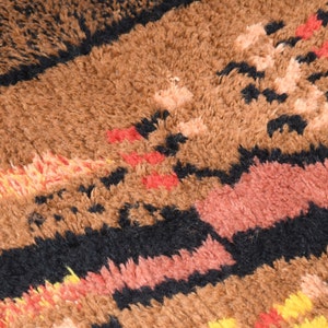 May include: Close-up of a brown, black, red, and yellow patterned rug with a fuzzy texture.