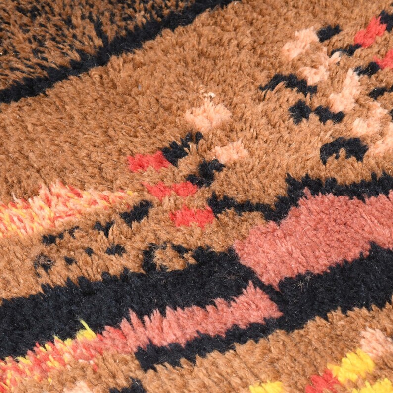 May include: Close-up of a brown, black, red, and yellow patterned rug with a fuzzy texture.