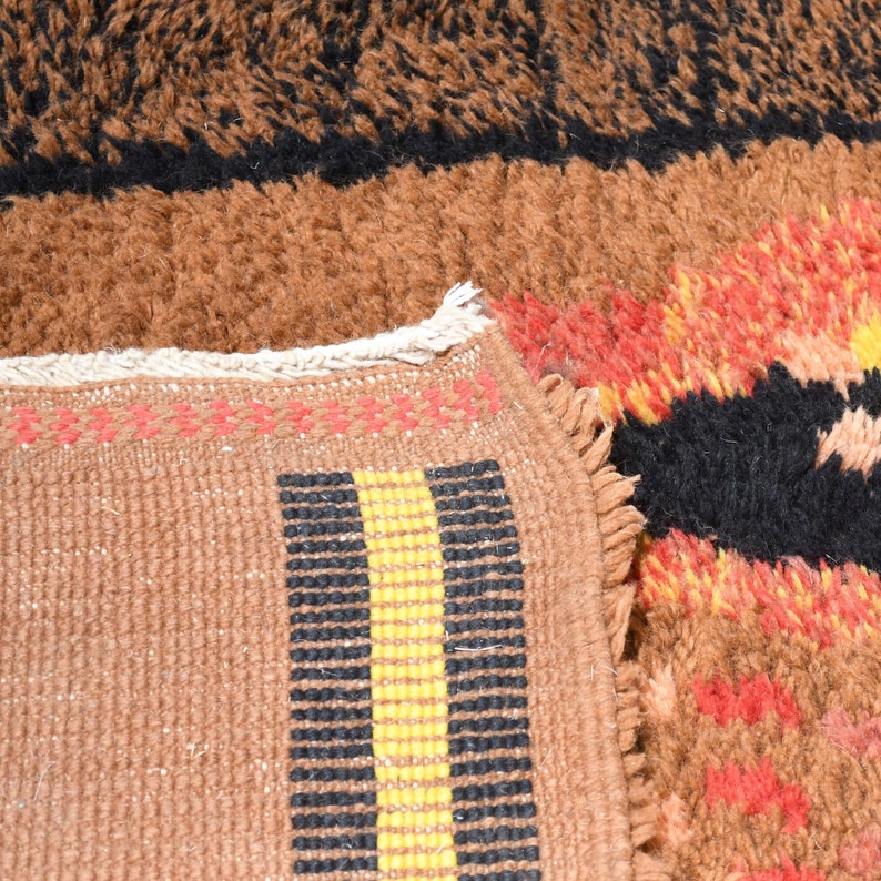 May include: Close-up of a brown and black patterned rug with a yellow and black stripe detail. The rug has a fringe border.