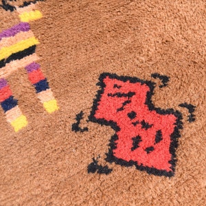 May include: A close-up of a brown rug with a red and black geometric design. The design is of a stylized animal, possibly a cat or a dog.