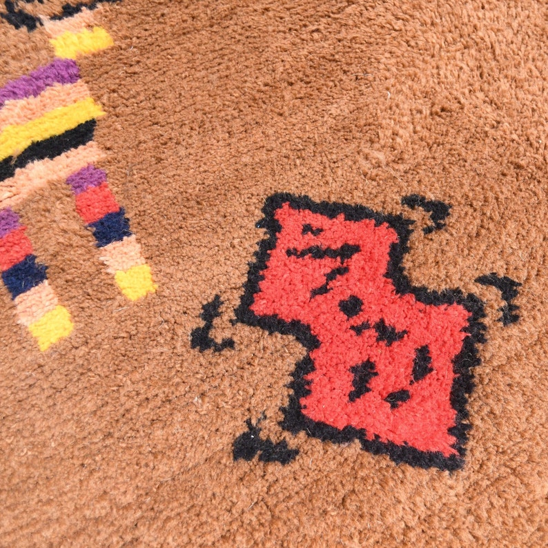 May include: A close-up of a brown rug with a red and black geometric design. The design is of a stylized animal, possibly a cat or a dog.