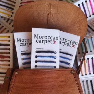 May include: Three cards with the text "Moroccan Carpet" and "Blue Shades" displayed on a brown leather surface. Each card shows a selection of blue yarn samples.