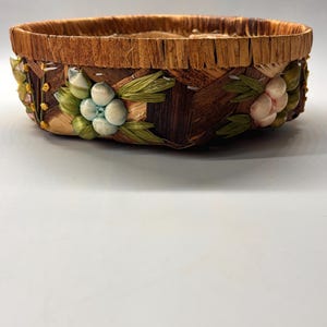 May include: A round woven basket with a brown and tan exterior. The basket is decorated with colorful flowers made from woven straw and fabric.