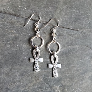 May include: A pair of silver earrings with an ankh pendant and a circle charm. Each earring has three small gold beads.