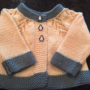 May include: A knitted baby cardigan in peach with a blue trim and penguin buttons.