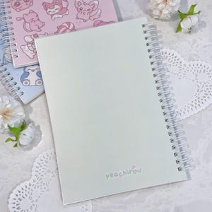 May include: A light green spiral bound notebook with the text "peachirou" printed on the back cover.