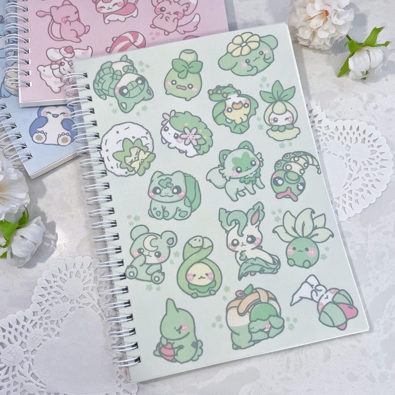 May include: A green spiral bound notebook with a variety of cute cartoon characters on the cover. The characters are green, white, and light pink and include a variety of plants and animals.