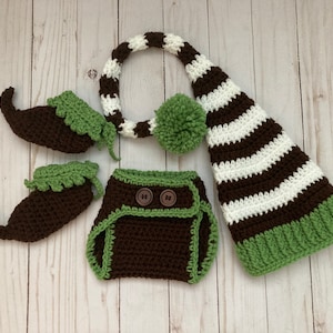 Puede incluir: Un conjunto de gnomo de crochet marrón y verde para un bebé recién nacido. El conjunto incluye un gorro, una cubierta de pañal y botines.
