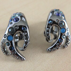 May include: A pair of silver tone clip-on earrings with a wave design and blue and clear rhinestones.