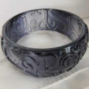 May include: A black plastic bangle bracelet with a decorative, swirling, embossed design.