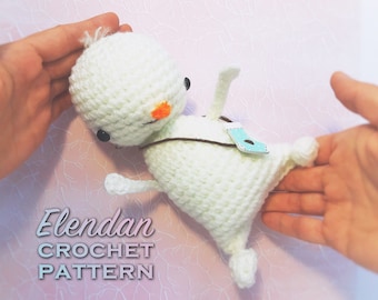 May include: White crocheted amigurumi toy with orange nose and black eyes. The toy is lying on a pink background with white floral pattern. The text "Elendan CROCHET PATTERN" is visible below the toy.