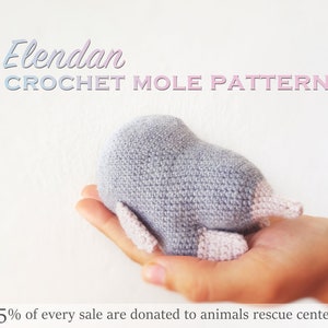Può includere: Un giocattolo di amigurumi a forma di talpa di colore grigio lavorato a uncinetto con dettagli rosa. Il giocattolo è tenuto nella mano di una persona. Il testo "Elendan CROCHET MOLE PATTERN" è nella parte superiore dell'immagine. Il testo "5% di ogni vendita viene donato ai centri di soccorso per animali" è nella parte inferiore dell'immagine.