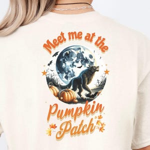 May include: Cream-colored t-shirt featuring a Halloween-themed graphic. The design includes a full moon, a howling wolf, pumpkins, and the text "Meet me at the Pumpkin Patch" in orange script. The shirt is made of a soft material.