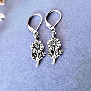 Könnte beinhalten: Ein Paar silberfarbene Ohrhänger. Jeder Ohrring hat ein Blumendesign mit detaillierten Blütenblättern und Blättern. Die Ohrringe haben einen Bügelverschluss und werden vor einem hellblauen Hintergrund präsentiert.