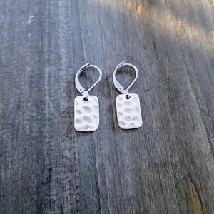 May include: A pair of silver earrings with a hammered rectangular design. The earrings have a simple hook fastening.