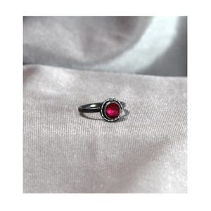 May include: A silver ring with a red gemstone set in a bezel setting.