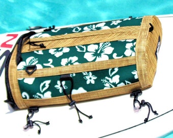 May include: A green and gold surfboard bag with a white hibiscus flower pattern. The bag has multiple straps and buckles.