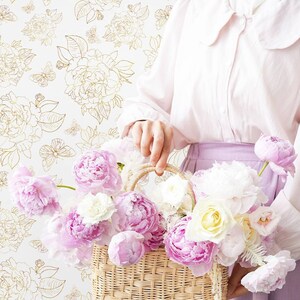 Woman holding a creel with peonies with a neutral toned floral wallpaper in background