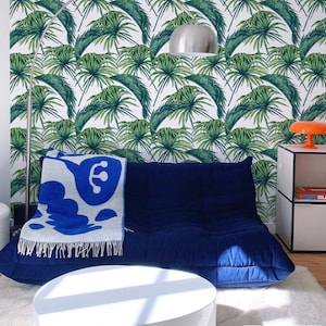 Modern and colorful bedroom with deep blue sofa, white coffee table and cream carpet. Modern tropical leaf pattern wallpaper on the wall.