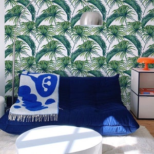 Modern and colorful bedroom with deep blue sofa, white coffee table and cream carpet. Modern tropical leaf pattern wallpaper on the wall.