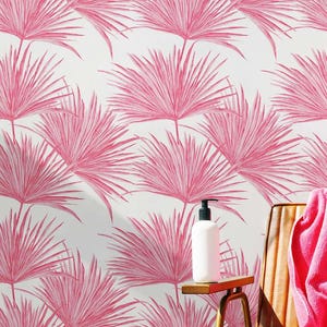 May include: Pink palm leaf wallpaper with a white background. A brown leather chair with a pink towel is in the foreground. A white bottle with a pump dispenser is on a wooden table.