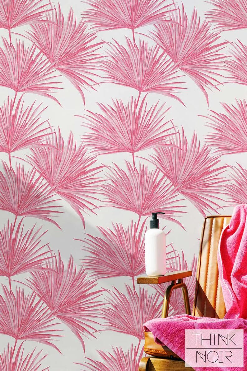 May include: Pink palm leaf wallpaper with a white background. A brown leather chair with a pink towel is in the foreground. A white bottle with a pump dispenser is on a wooden table.