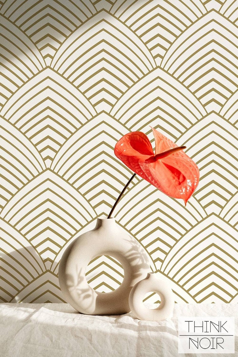Red flower in a cream color design vase on a linen table cloth with a modern art deco inspired pattern wallpaper in the background.
