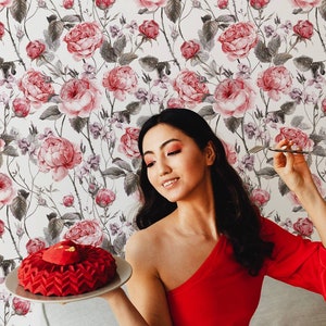 Woman in a red dress posing with a red cake in a room with rose patterned wallpaper.