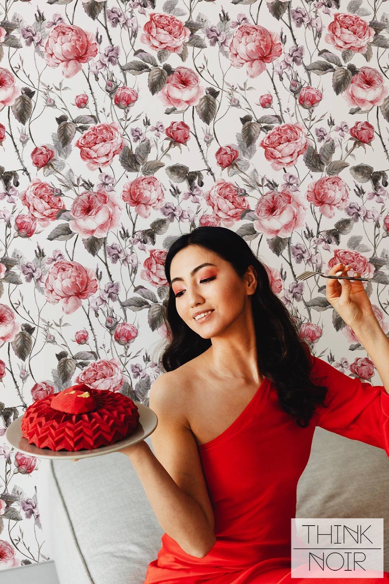 Woman in a red dress posing with a red cake in a room with rose patterned wallpaper.